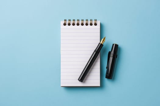 Top view of notebook and fountain pen on blue background