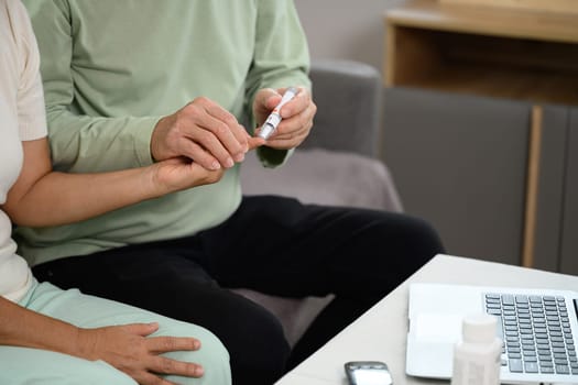 Elderly man checking blood sugar of his diabetic wife at home. Elderly healthcare concept.