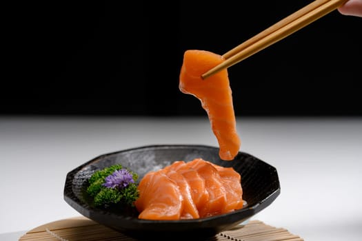 Fresh sliced salmon sashimi served with parsley leaf on a black Japanese style plate.