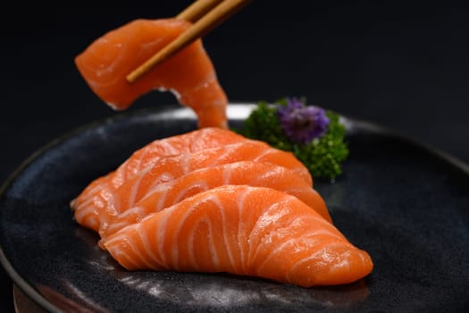 Chopsticks with sliced raw salmon over black background. Close up shot.