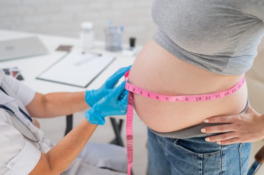 Doctor measuring the volume of a pregnant woman's abdomen using a tape in inches