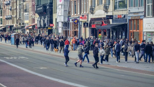 Amsterdam Netherlands 21 April 2024, A diverse crowd of people walks briskly down a bustling city street lined with towering buildings