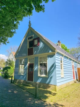 A charming small blue house stands out with its vibrant red door, creating a picturesque scene in a quaint setting. Broek in Waterland Netherlands 21 April 2024