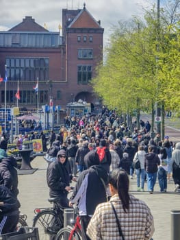 Amsterdam Netherlands 21 April 2024, A bustling street filled with a diverse group of people walking together in an organized yet fluid motion, creating a dynamic and vibrant scene.