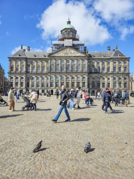 Amsterdam Netherlands 21 April 2024, A diverse group of people wander aimlessly in front of a colossal, majestic building. palace of Dam square