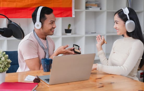 A young gay man and his girlfriend use a laptop and microphone to stream podcast audio at a studio talking about gender liberation..