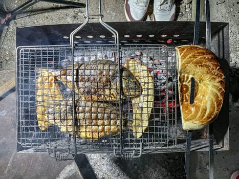 Authentic outdoor cooking scene with two grilled fishes on the grid over charcoals. Focus on the mouth-watering seafood.