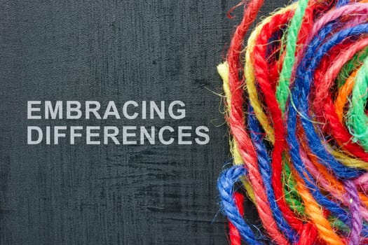 Words Embracing differences next to ball of colored threads.