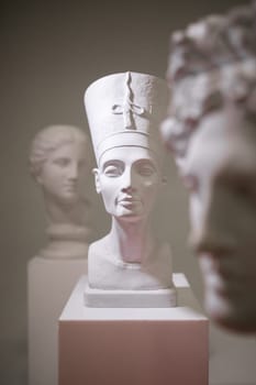 A white sculpture bust of Queen Nefertiti on a white background, showcasing the elegant beauty and history of Ancient Egypt.