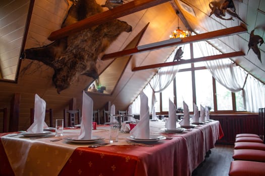 Long table in rustic restaurant with white tablecloths and animal trophies on walls and chandelier on ceiling.