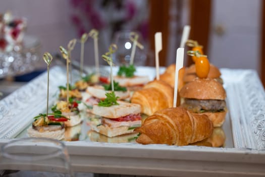 Variety of sandwiches, croissants, burgers on silver tray with mirror base, perfect for catered event indulgence.