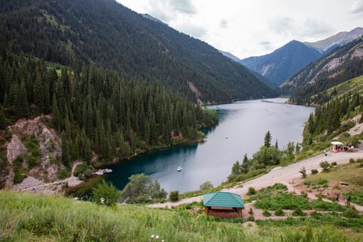 Lake surrounded by snowy mountains, crystal clear water, blue sky, hazy clouds, fresh air. Small house on shore of lake.