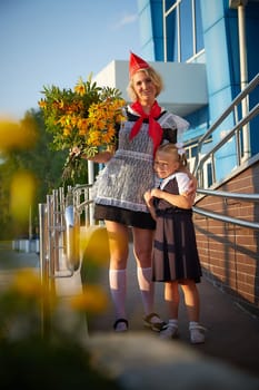 Young and adult schoolgirl on September 1 with flowers. Generations of schoolchildren of USSR and Russia. Female pioneer in red tie and October girl in modern uniform. Daughter and Mother having fun