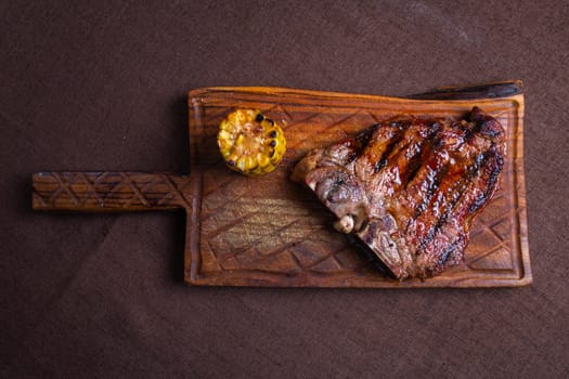 A juicy and tender grilled steak with a side of corn on the cob, served on a rustic wooden cutting board.