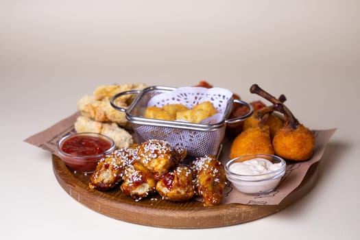 A variety of fried chicken wings, potato balls, and cheese sticks with dipping sauces on a wooden platter.