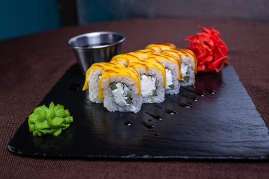 A plate of sushi with cream cheese, cucumber, and eel topped with yellow sauce, wasabi paste, and a flower garnish