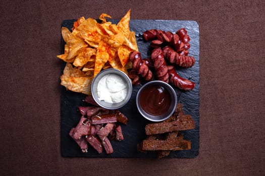 A top-down view of a tantalizing plate featuring bread, savory meat, delicious sausage, crispy chips, and flavorful dip.