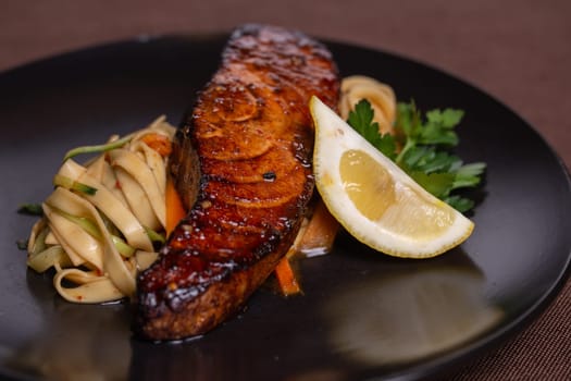 A mouthwatering and nutritious dish featuring grilled salmon, lemon, and fresh vegetables on a sleek black plate.