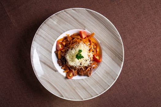 Top view of a delicious plate of beef stew with pasta, tomatoes, and cheese topping, perfect for lunch or dinner.