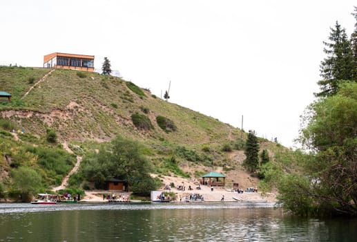 The lake is surrounded by green hills and the water is crystal clear. There is a building on the hill and trees on the shore.