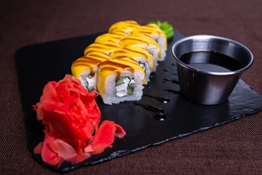 A plate of sushi with cream cheese, cucumber, and eel topped with yellow sauce, wasabi paste, and a flower garnish