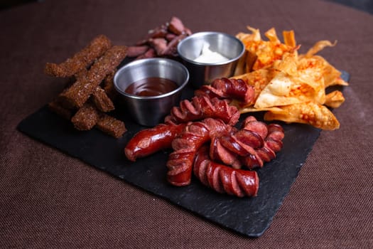 A top-down view of a tantalizing plate featuring bread, savory meat, delicious sausage, crispy chips, and flavorful dip.