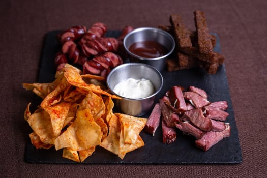 A top-down view of a tantalizing plate featuring bread, savory meat, delicious sausage, crispy chips, and flavorful dip.