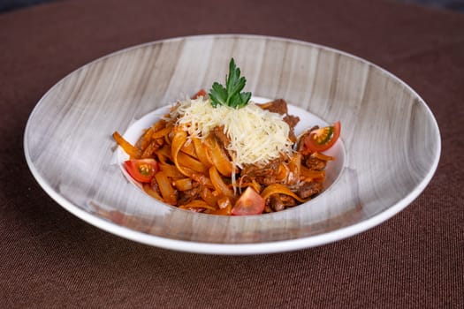 Top view of a delicious plate of beef stew with pasta, tomatoes, and cheese topping, perfect for lunch or dinner.