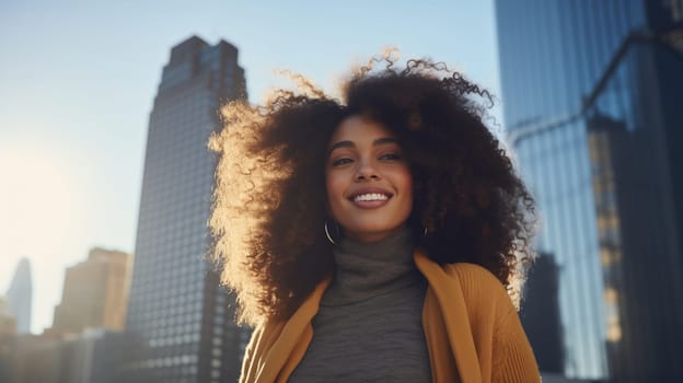 Portrait of beautiful smiling modern African young woman with lush curly hair standing in sunny city