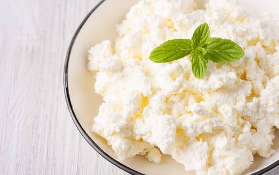 Cottage cheese in a plate on a white table, with copy space for text.