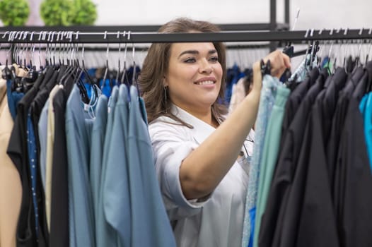 Portrait of a fat woman in a plus size store through hangers with clothes