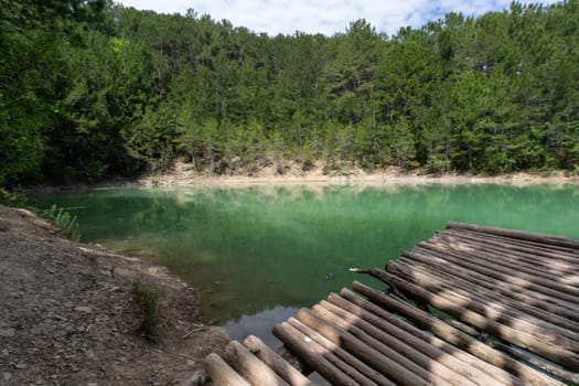 A wooden bridge spans a body of water, with trees in the background. The scene is serene and peaceful, with the water reflecting the surrounding trees and the bridge