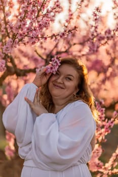 Woman blooming peach orchard. Against the backdrop of a picturesque peach orchard, a woman in a long white dress enjoys a peaceful walk in the park, surrounded by the beauty of nature