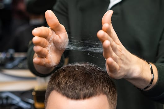 Hairdresser adjusts freshly cut hair of client in barbershop closeup. Careful stylist tousles haircut serving man in grooming salon