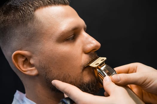 Young man undergoes mustache hair-cutting in luxury barber-shop closeup. Hairdresser uses shaver machine to care of client facial hair