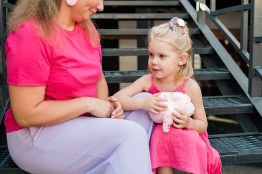 Blonde little girl with cochlear implant playing with her mother outdoor. Hear impairment deaf and health concept. Diversity and inclusion. Copy space.