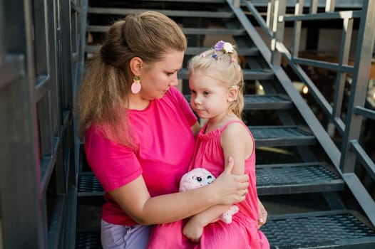 Blonde little girl with cochlear implant playing with her mother outdoor. Hear impairment deaf and health concept. Diversity and inclusion. Copy space.