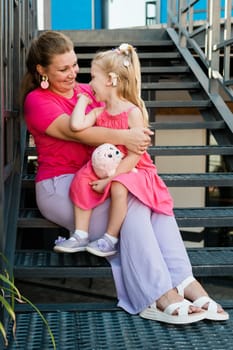 Deaf child with cochlear implant for hearing audio and aid for impairment having fun and laughs with mother outdoor in summer. Sound fitting device to help with communication listening and interaction.