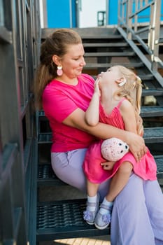 Deaf child with cochlear implant for hearing audio and aid for impairment having fun and laughs with mother outdoor in summer. Sound fitting device to help with communication listening and interaction.