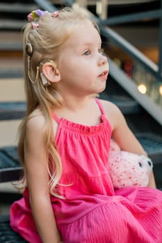 Child girl walks and have fun outdoor with cochlear implant on the head. Hearing aid and treatment concept. Copy space vertical.