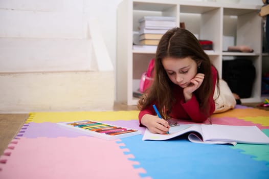 Smart small school girl studying at home, handwriting in notebook. Hardworking focused little girl child drawing picture, doing homework lessons alone, feel motivated at learning, education concept