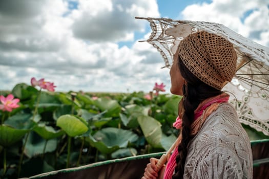 A woman wearing a hat and holding an umbrella is looking at a field of pink flowers. The scene is peaceful and serene, with the woman taking in the beauty of the flowers