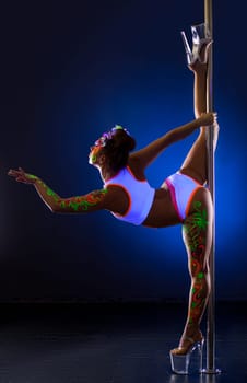 Pole dance. Flexible girl with luminous bodyart posing