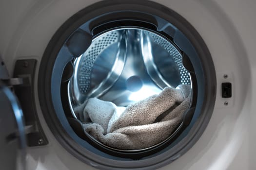 Opened washing machine drum with towel. Closeup. Front view. Washing dirty clothes in the washer. High quality photo