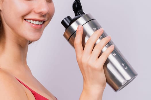 Closeup side view of a sportive female after training who drinking fresh water from sport bottle