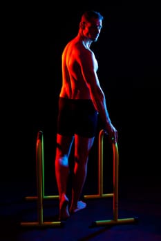 Front and side view photo of strong young man exercising on parallel bars in studio.