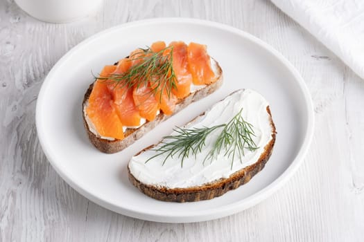 Rye sandwich with salmon and cream cheese on white wooden table.