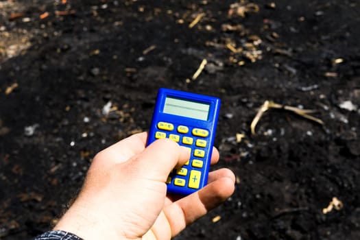 Blue calculator in dark soil, burnt ground after a fire