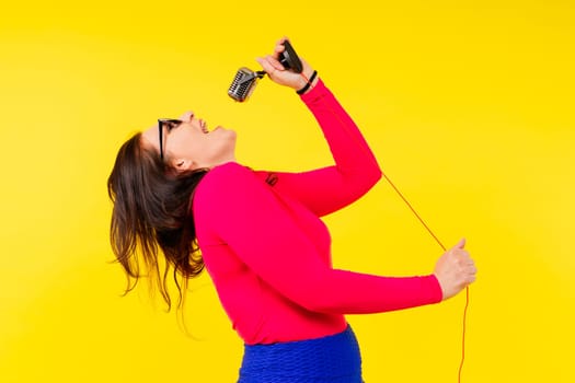 Woman in sport clothes sings into wired microphone and claps her hands on a yellow background