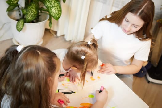 Young mother or babysitter, little daughter, sister teenager girl drawing at table in room. Painting, doing homework. Family enjoying leisure at home